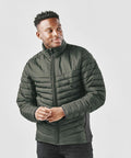 A person wearing a dark green Stormtech ST225 quilted jacket with a full front zipper stands against a plain white background.