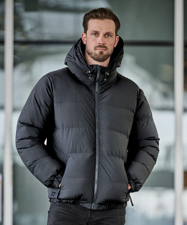 A person stands in front of a building wearing a black Stormtech ST227 with the hood down, hands in pockets.