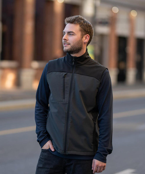 A man with short hair and a beard wears the Stormtech Cascades softshell gilet on a city street, looking to his left with one hand in his pocket against blurred urban buildings.