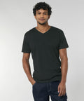 A man with curly hair is wearing a black V-neck T-shirt (SX021) by Stanley/Stella and blue jeans against a plain background.
