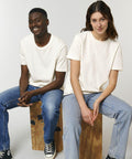 Two people sitting on Stanley/Stella SX141, both wearing light-colored t-shirts and blue jeans, smiling and looking into the camera against a plain background.