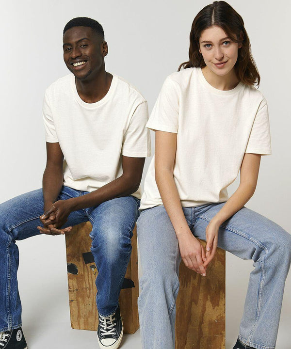 Two people sitting on Stanley/Stella SX141, both wearing light-colored t-shirts and blue jeans, smiling and looking into the camera against a plain background.