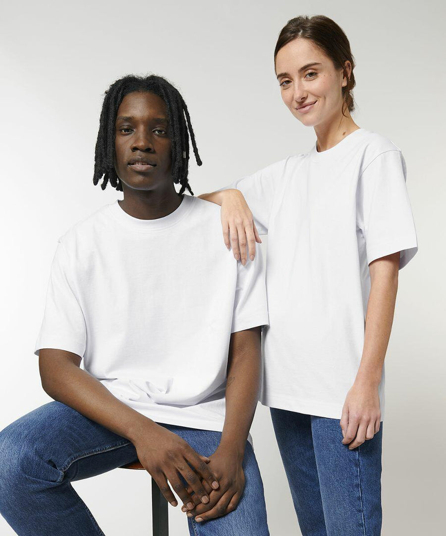 Two people wearing white Stanley/Stella SX142 t-shirts and blue jeans pose for a photo, with one person sitting on a stool and the other standing beside them.