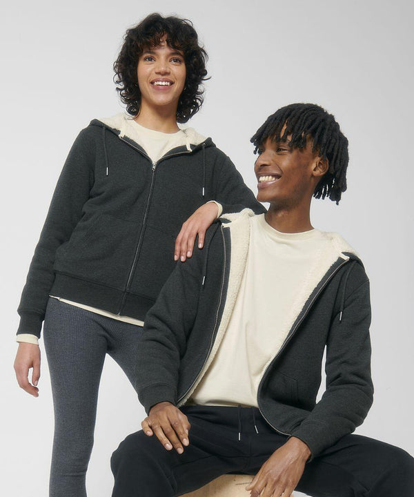 Two individuals wearing dark SX222 zip-up hoodies from Stanley/Stella and light-colored t-shirts, smiling, against a white background. One stands while the other sits on a stool.