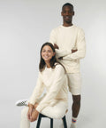 Two people are posing in off-white casual outfits. The person seated is wearing a Stanley/Stella SX230 long-sleeve shirt and pants, while the person standing is wearing a Stanley/Stella SX230 long-sleeve shirt and shorts.