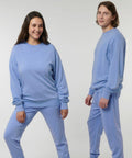 Two individuals are wearing matching light blue Stanley/Stella SX231 sweatshirts and sweatpants. The person on the left is smiling, while the person on the right has a neutral expression. They are standing against a plain background.