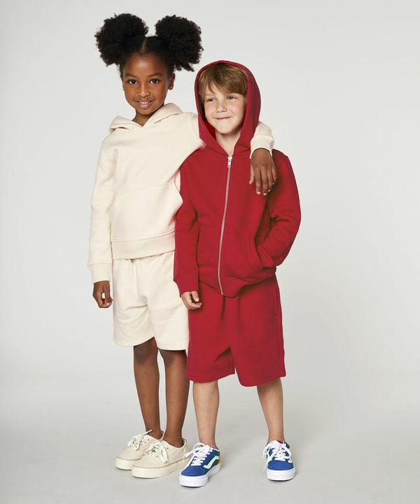 Two children stand together. One wears a beige SX232 by Stanley/Stella hoodie and shorts, while the other wears a red SX232 by Stanley/Stella hoodie and matching shorts. Both are smiling and have their arms around each other.