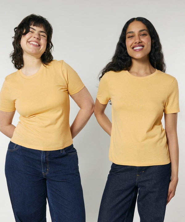 Two women stand side by side, smiling and wearing yellow SX234 t-shirts by Stanley/Stella and dark jeans against a plain background.