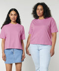 Two individuals wearing similar pink SX235 t-shirts by Stanley/Stella. The person on the left wears a blue denim skirt, while the person on the right wears light blue jeans. Both standing against a plain background.