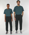 Two individuals wearing matching dark green Stanley/Stella SX242 t-shirts and black sweatpants stand side by side against a plain background, smiling at the camera.