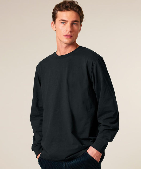A man with short brown hair wears the Stanley/Stella Freestyler long sleeve (STTU200) and dark trousers. He stands against a neutral background, left hand in his pocket, looking directly at the camera.