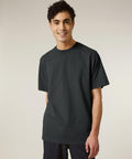 A young person with short dark hair smiles at the camera indoors, wearing a Stanley/Stella Freestyler Vintage (STTU073) t-shirt and dark trousers against a neutral background.
