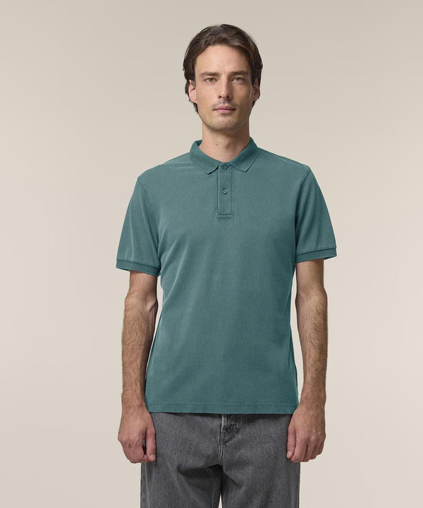 A man with short brown hair, wearing the Stanley/Stella Coaster Vintage (STPU252) teal polo shirt and grey jeans, stands facing forwards against a plain light beige background.