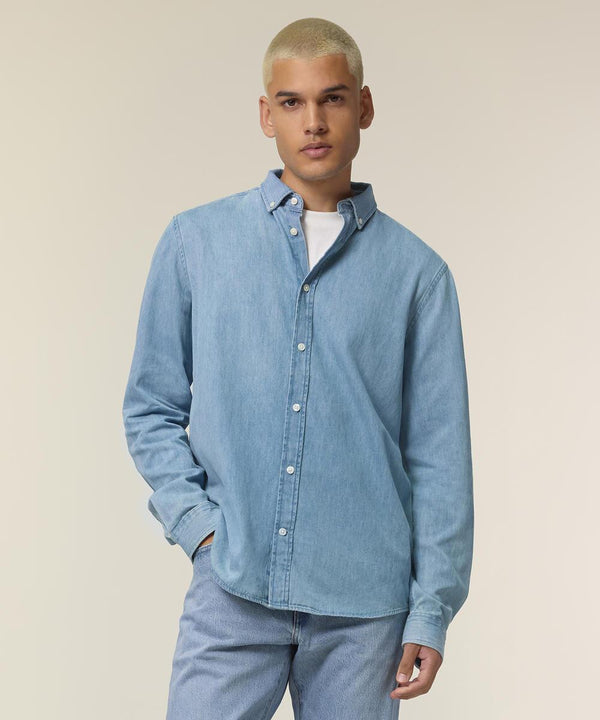 A person with short, bleached blond hair wears the Stanley/Stella Stanley denim shirt (STWM967) over a white T-shirt and light blue jeans, standing against a plain, light-coloured background.