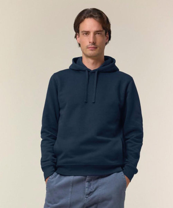 A man with short brown hair stands against a plain light background, wearing the Stanley/Stella Sounder (STSU229) dark blue hoodie and matching blue trousers, hands in pockets and a neutral expression.