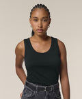 A person with plaited hair models the Stanley/Stella Stella Ava (STTW963) black sleeveless top and black jeans with a belt, standing against a plain light background and looking directly at the camera.