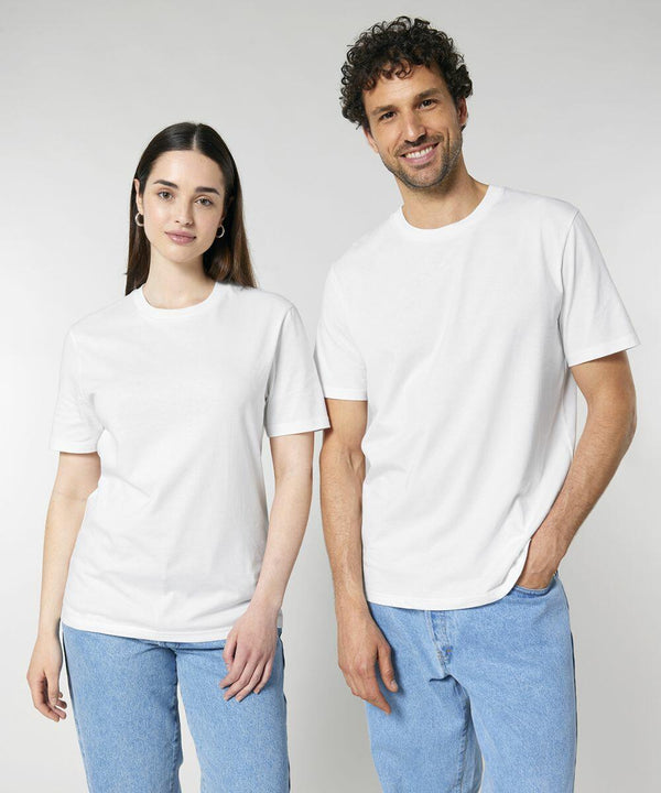 A woman and a man stand side by side wearing plain white Stanley/Stella SX701 t-shirts and light blue jeans. The background is plain and light gray.