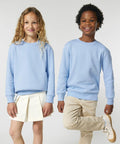 Two children standing side by side, both wearing SX704 sweatshirts from Stanley/Stella. The child on the left has long curly hair and a white skirt. The child on the right has short curly hair and light-colored pants.