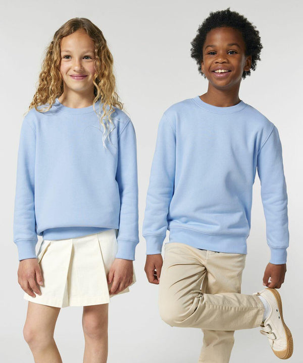 Two children standing side by side, both wearing SX704 sweatshirts from Stanley/Stella. The child on the left has long curly hair and a white skirt. The child on the right has short curly hair and light-colored pants.