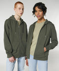 Two people standing side by side, both are wearing Stanley/Stella SX712 green zip-up hoodies, light-colored t-shirts, and light blue jeans, against a plain background.