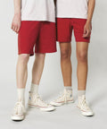 Two individuals wearing white shirts, red shorts, white socks, and Stanley/Stella SX722 sneakers with blue logos, standing against a plain backdrop.