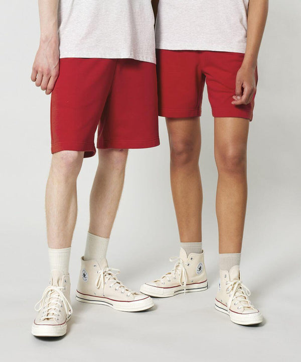 Two individuals wearing white shirts, red shorts, white socks, and Stanley/Stella SX722 sneakers with blue logos, standing against a plain backdrop.