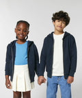A young girl and boy, both wearing navy SX749 zip-up hoodies by Stanley/Stella, hold hands. The girl also wears a light blue shirt and white skirt, while the boy has on a white shirt and blue jeans.