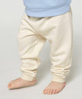 A child wearing Stanley/Stella SX767 cream-colored pants and a blue top is standing barefoot on the floor.