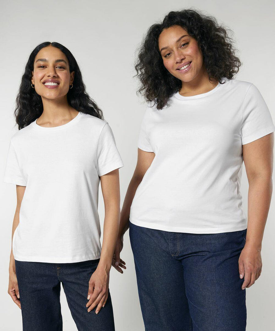 Two women are standing side by side, both wearing Stanley/Stella SX768 white t-shirts and blue jeans, smiling at the camera against a plain background.