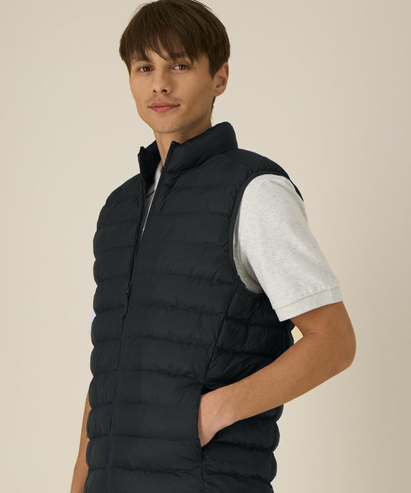 A person with short brown hair wears the Stanley/Stella Stanley Climber 2.0 (STJM189) light grey short-sleeve t-shirt and a black puffer gilet, standing with one hand in the gilet pocket against a plain, light background.