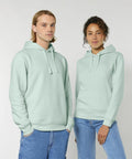 Two people wearing light green Stanley/Stella SX789 hoodies stand side by side against a plain background. Both have their hands in the kangaroo pockets of their hoodies.