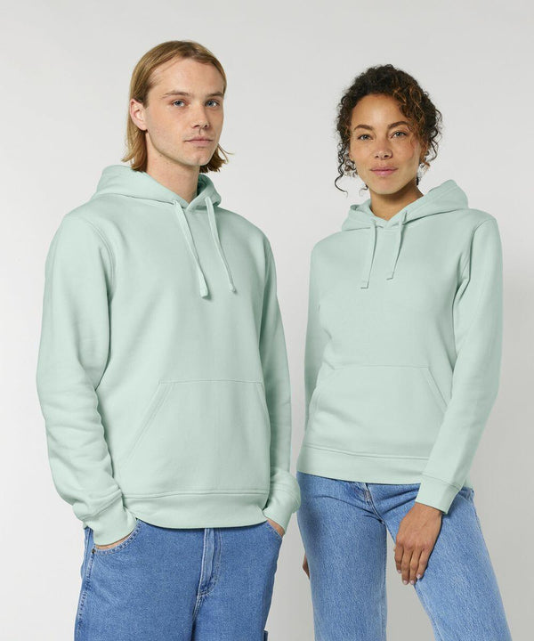 Two people wearing light green Stanley/Stella SX789 hoodies stand side by side against a plain background. Both have their hands in the kangaroo pockets of their hoodies.