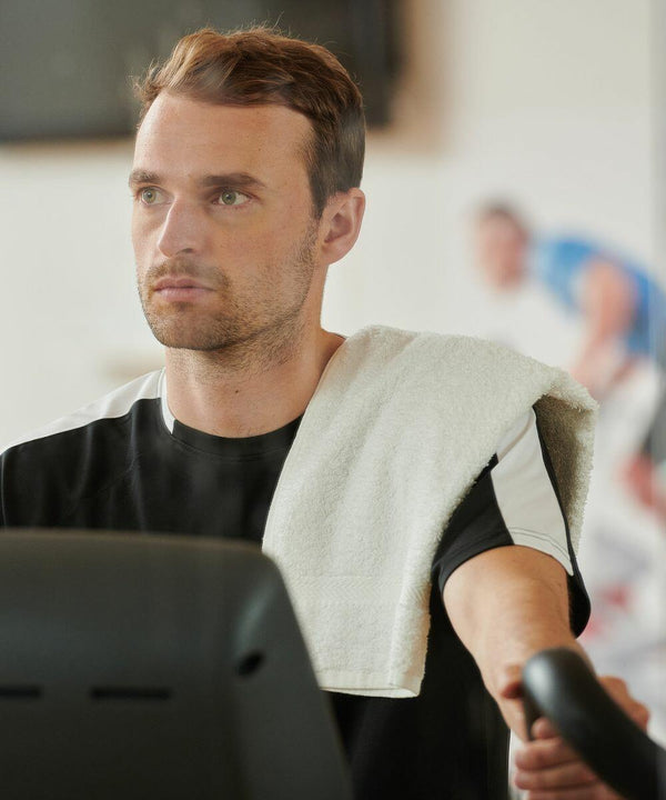 Man exercising on a stationary bike with a Towel City TC002 over his shoulder, looking forward.