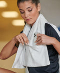 A person with a white towel around their neck places a Towel City TC007 into a pocket on the towel, wearing a black athletic shirt.
