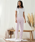 A woman stands in a room wearing a white t-shirt, pink and white striped pants, and Towel City TC053 slippers. She is next to a wooden bench with a beige throw and pampas grass in a vase.