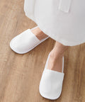 Person wearing white TC066 slippers and a white robe from Towel City, standing on a wooden floor.