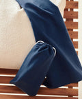 A Towel City quick-dry beach towel in dark blue is draped over the edge of a textured off-white mattress, with its matching fabric bag featuring a white drawstring resting on a wooden slatted surface nearby.
