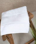 A Towel City TC504 is neatly folded and placed on a rustic wooden stool next to a green plant.
