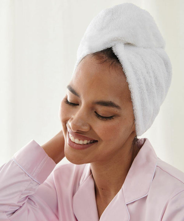 A person with a Towel City TC933 wrapped around their hair smiles contentedly. They are wearing a light pink pajama top and have their eyes closed.
