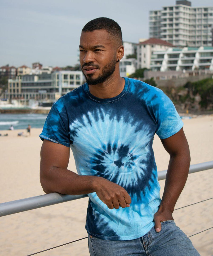 A man in a Colortone TD02M stands by a railing at a beach, with buildings in the background.
