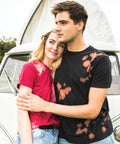 A couple stands in front of a vehicle, with the man wearing a black Colortone TD09M and hugging the woman, who is wearing a red Colortone TD09M.