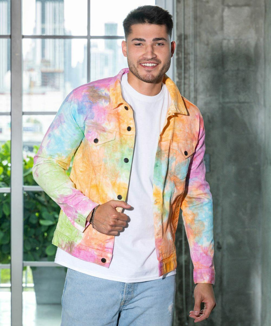 A man in a Colortone TD32M tie-dye jacket and white t-shirt stands indoors near a large window.