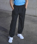 Person wearing a light blue TL047 by Tombo, black track pants, and white sneakers, standing with hands in pockets on a concrete surface.