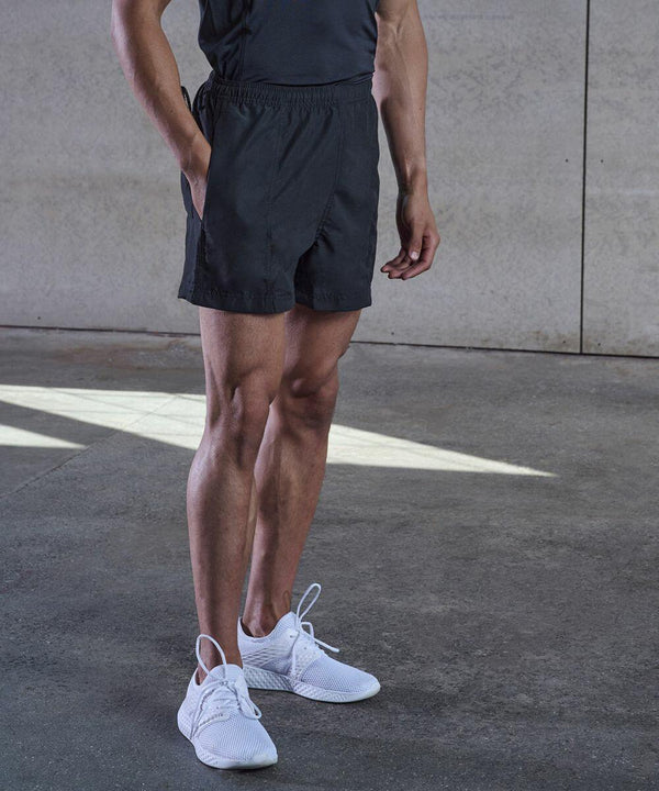 A person wearing a dark shirt, black shorts, and white Tombo TL080 athletic shoes stands on a concrete floor with one hand in their pocket.