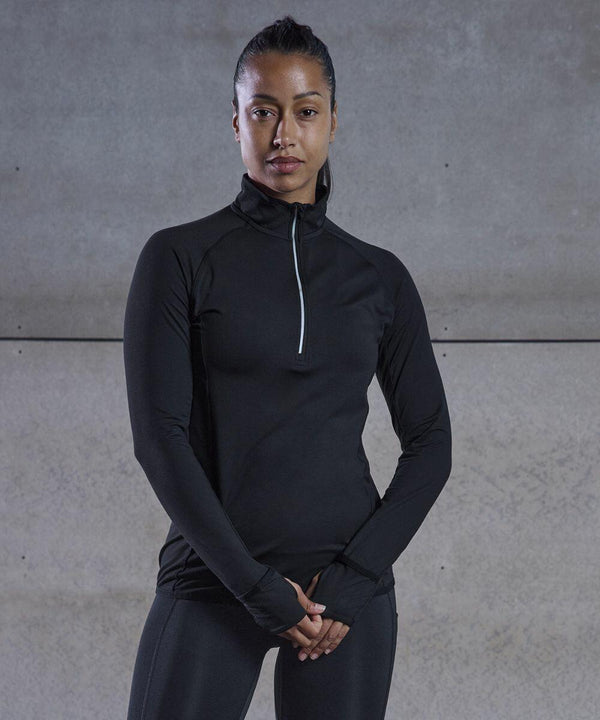 A person stands against a plain background wearing a black Tombo TL563 athletic top with a zip collar.