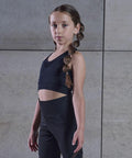 Young girl with long braids, wearing Tombo TL697, stands against a gray tiled wall.