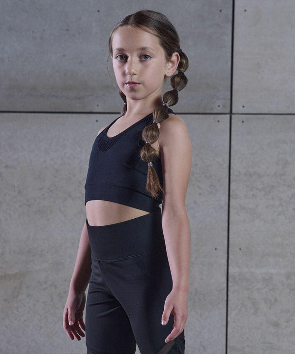 Young girl with long braids, wearing Tombo TL697, stands against a gray tiled wall.