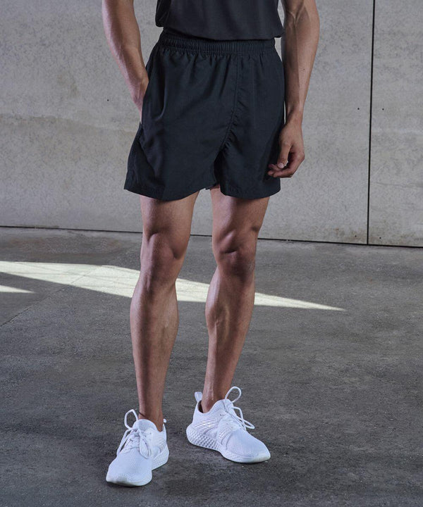 A person wearing black Tombo TL800 athletic shorts, a dark shirt, and white sneakers stands on a concrete floor with a neutral background.