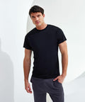 A man standing against a white background, wearing a black Tri-Dri TR010 t-shirt and gray pants, looking at the camera with a neutral expression.
