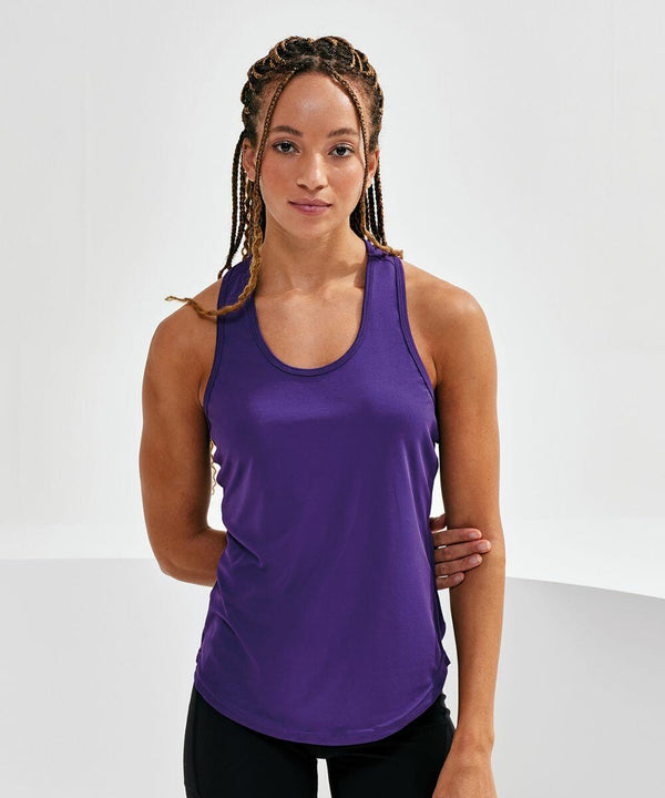 Person with braided hair wearing a purple sleeveless top and black pants standing against a plain white background, looking at the camera. Outfitted in the TR027 by Tri-Dri.